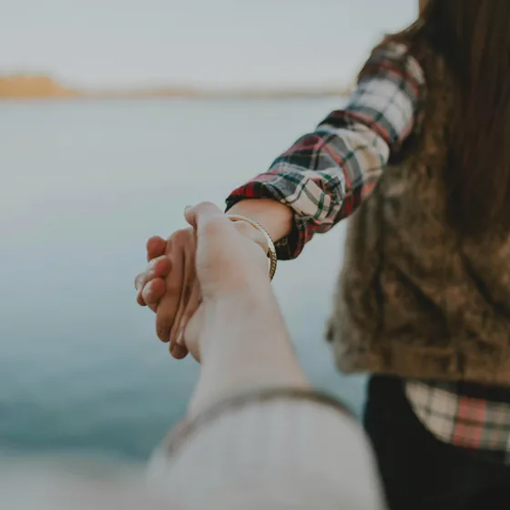 Two people holding hands by the water.